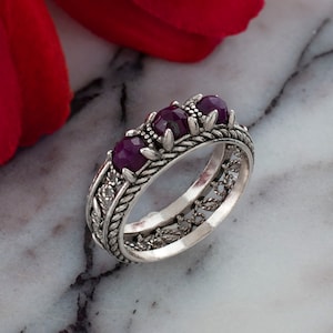 May include: A silver ring featuring three purple gemstones set in an intricate filigree design.