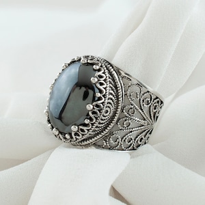 May include: A silver ring with an oval black gemstone set in a filigree design.