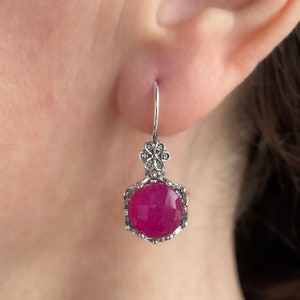 May include: Silver dangle earrings featuring a pink gemstone and a floral design.