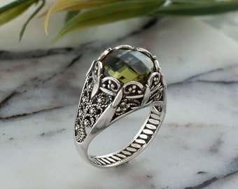 May include: A silver ring with an ornate design featuring a large, round, green gemstone.