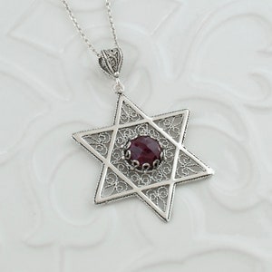 Peut inclure: Un collier avec un pendentif en forme d'étoile de David en filigrane argenté avec une pierre précieuse rouge au centre.