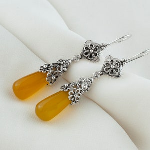 May include: A pair of silver dangle earrings with yellow teardrop-shaped stones and intricate floral designs.
