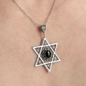Könnte beinhalten: Eine silberne Kettenkette mit einem silbernen Davidstern-Anhänger mit einem schwarzen Edelstein in der Mitte.