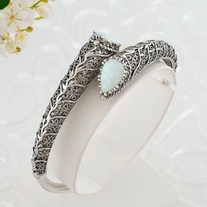 May include: A silver bangle bracelet with an intricate filigree design and two white opal stones.