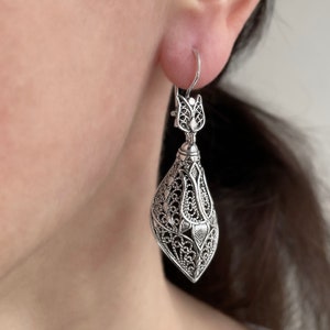May include: Silver filigree earrings with a teardrop shape and intricate floral designs.