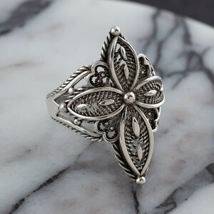 May include: A silver ring with a delicate, intricate floral design. The ring is made of sterling silver and features a filigree pattern.