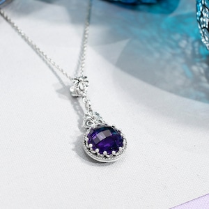 May include: A silver necklace with a purple gemstone pendant. The pendant is surrounded by a decorative silver frame.