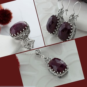 Op de afbeelding: Een robijn-korund sieradenset met een ring, hanger en oorbellen. De set heeft een dieprode edelsteen met ingewikkelde zilveren filigraan details.