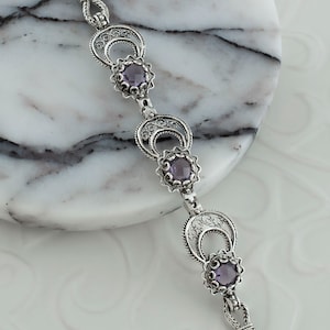 May include: A silver bracelet with three amethyst gemstones set in filigree designs. The bracelet has a chain link closure.