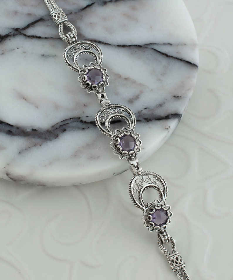 May include: A silver bracelet with three amethyst gemstones set in filigree designs. The bracelet has a chain link closure.
