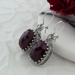 Peut inclure: Une paire de boucles d'oreilles pendantes en argent avec des gouttes de pierres précieuses rouge foncé. Les boucles d'oreilles ont un design filigrané détaillé.