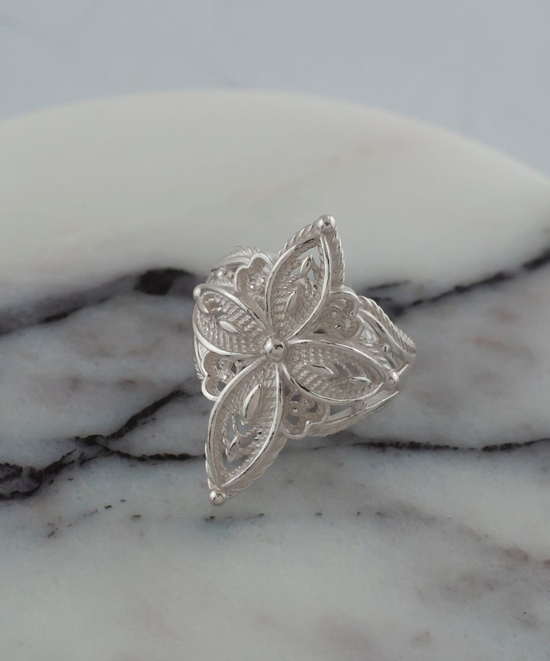 May include: A silver filigree ring with a flower design. The ring is delicate and intricate, with a floral pattern that is reminiscent of a vintage style.