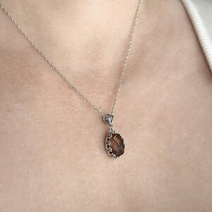 May include: A silver chain necklace with a brown oval gemstone pendant. The pendant has a detailed silver frame.