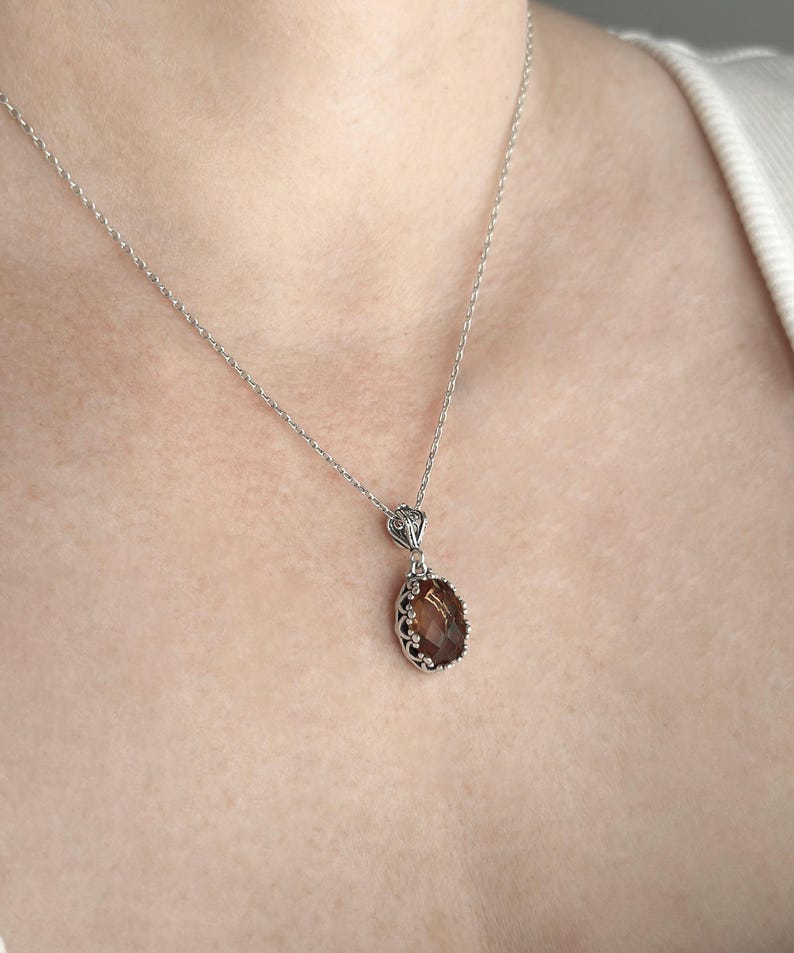 May include: A silver chain necklace with a brown oval gemstone pendant. The pendant has a detailed silver frame.