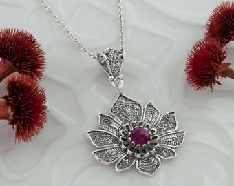 May include: A silver necklace with a filigree flower pendant featuring a purple gemstone in the centre.