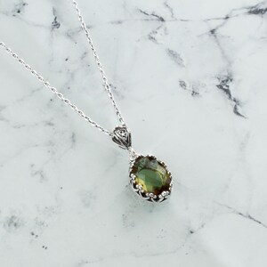 May include: A silver chain necklace with a green gemstone pendant. The pendant is oval shaped and has a detailed silver frame.