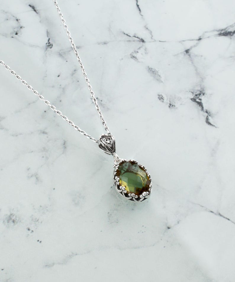 May include: A silver chain necklace with a green gemstone pendant. The pendant is oval shaped and has a detailed silver frame.