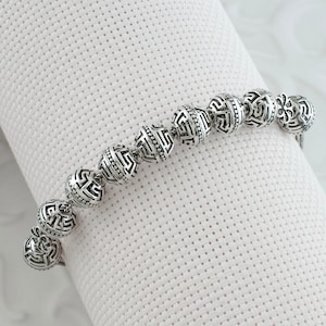May include: A silver bracelet with a series of round beads, each with a detailed geometric pattern. The beads are connected by a thin silver chain.