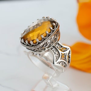 May include: A silver ring with an intricate filigree design and a large, oval-shaped amber gemstone.