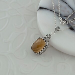 May include: A silver necklace with a brown gemstone pendant. The pendant is set in a filigree design and has a faceted gemstone.