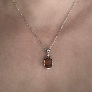May include: A silver chain necklace with a brown oval pendant. The pendant has a detailed silver frame.