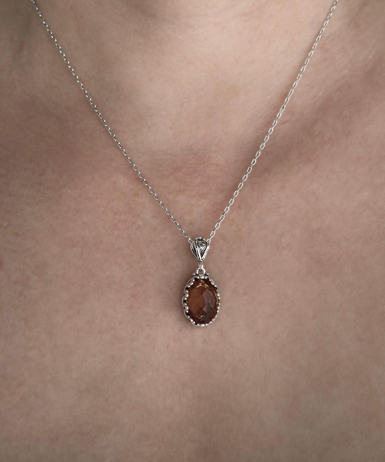 May include: A silver chain necklace with a brown oval pendant. The pendant has a detailed silver frame.