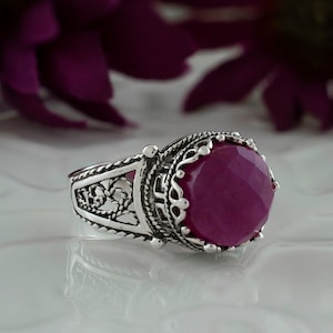 Könnte beinhalten: Ein silberner Ring mit einem verzierten Design und einem großen, facettierten, tiefrosa Edelstein.