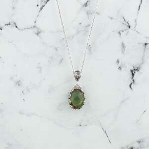 May include: A silver chain necklace with a green gemstone pendant. The pendant is oval shaped and has a silver filigree design around the edge.