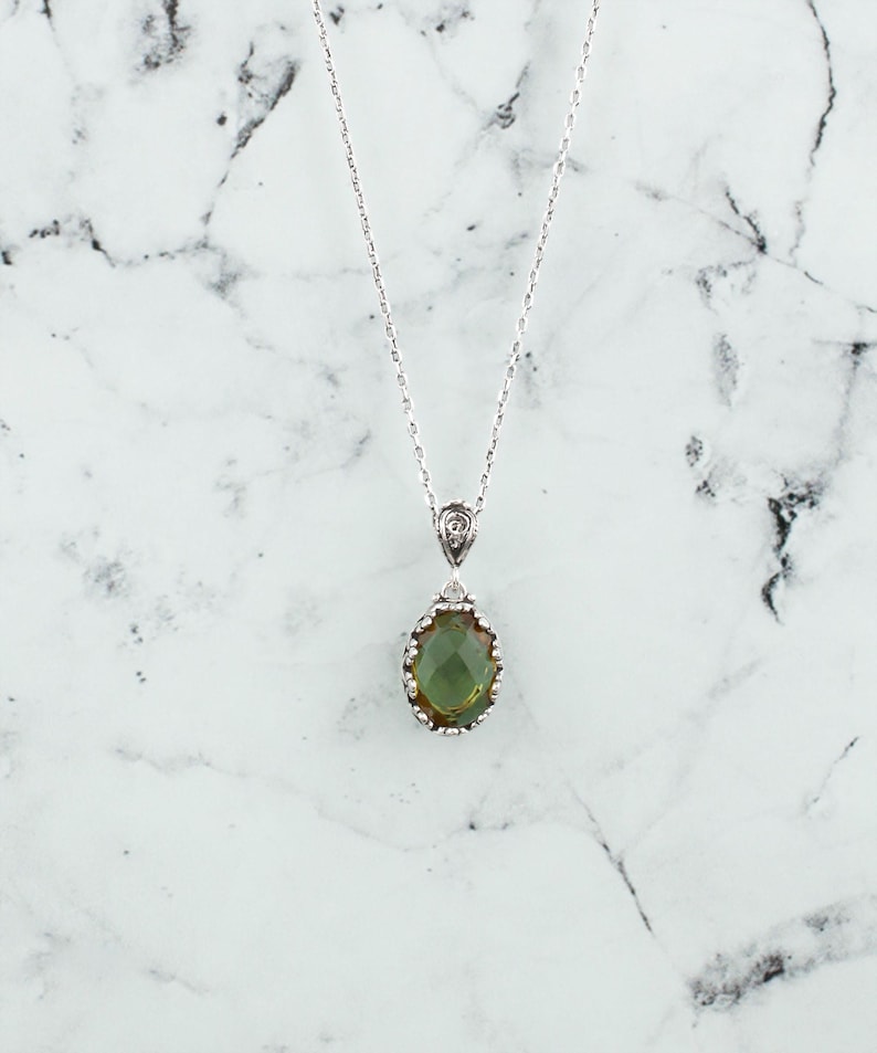 May include: A silver chain necklace with a green gemstone pendant. The pendant is oval shaped and has a silver filigree design around the edge.