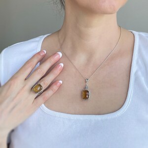 May include: A silver necklace with a brown gemstone pendant and a matching ring. The pendant and ring feature intricate silver designs.