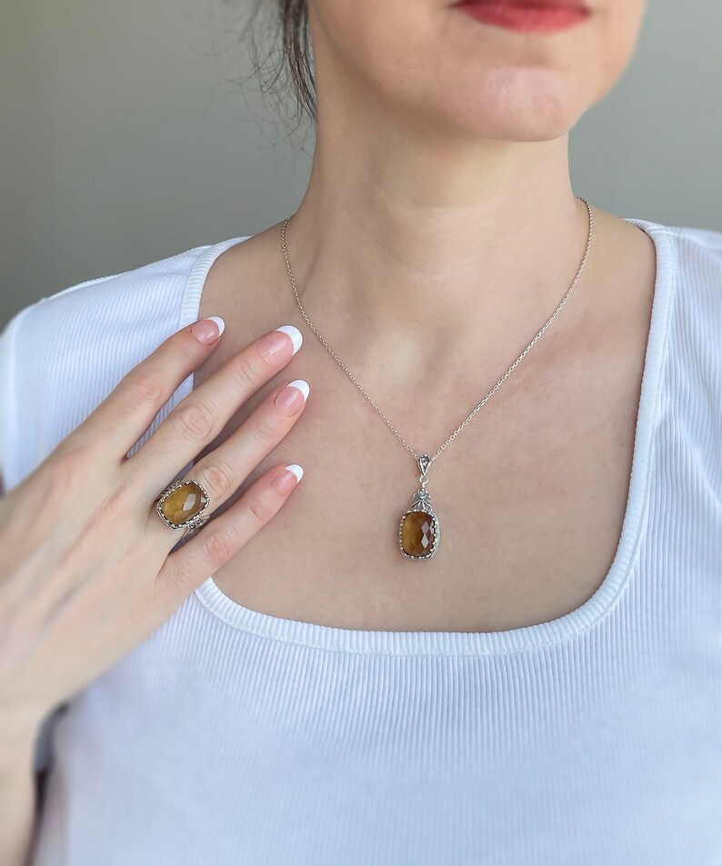May include: A silver necklace with a brown gemstone pendant and a matching ring. The pendant and ring feature intricate silver designs.