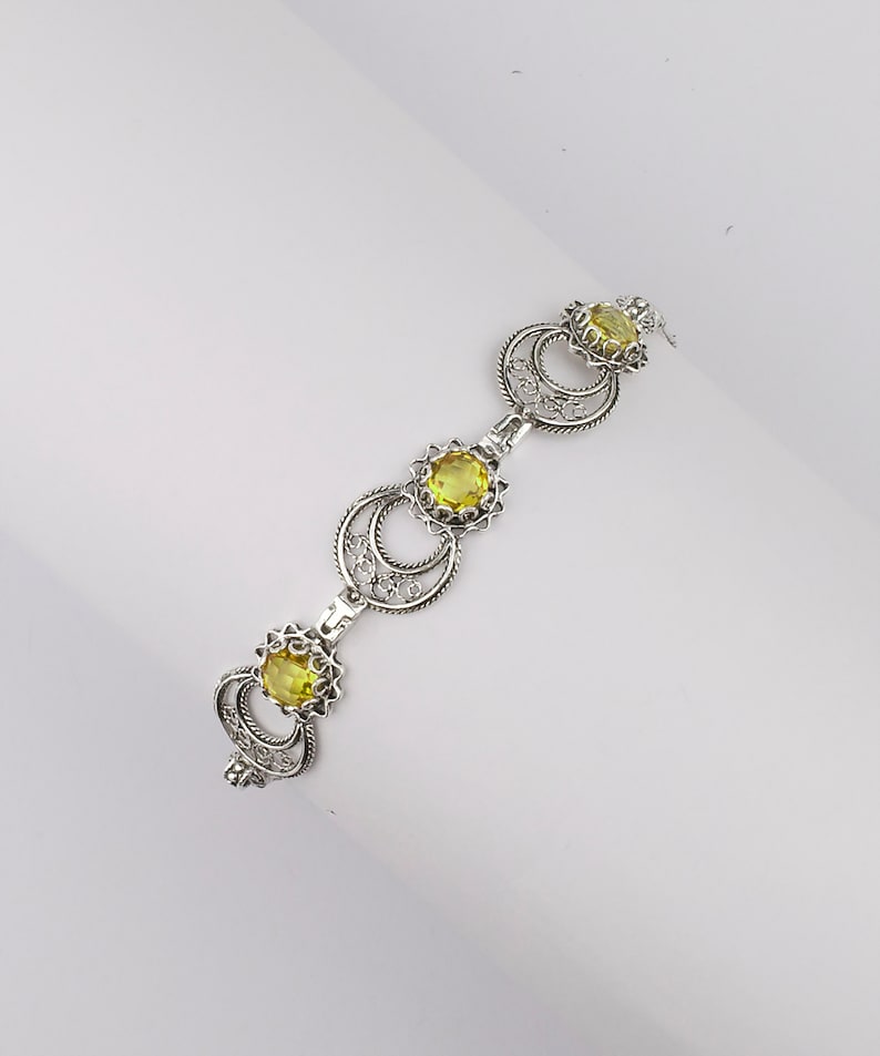May include: A silver bracelet with three yellow gemstones set in intricate filigree designs.