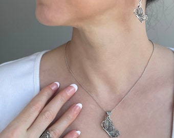 May include: A silver necklace and earrings set featuring a delicate butterfly design. The necklace has a pendant with a detailed butterfly charm, while the earrings feature a dangling butterfly design.