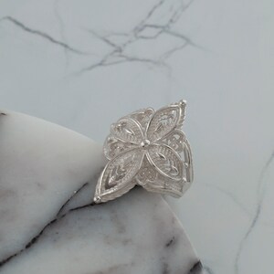May include: A silver filigree ring with a flower design. The ring is delicate and intricate, with a floral pattern that is reminiscent of lace.