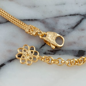 K&ouml;nnte beinhalten: Goldkette Armband mit einem zarten Blumenanh&auml;nger und einem Karabinerverschluss.