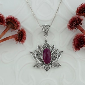Op de afbeelding: Een zilveren filigrain lotusbloem hanger ketting met een dieppaarse edelsteen in het midden.