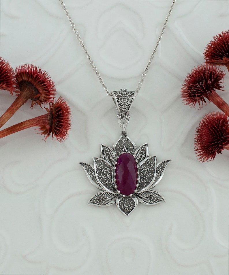Op de afbeelding: Een zilveren filigrain lotusbloem hanger ketting met een dieppaarse edelsteen in het midden.