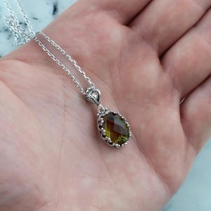 May include: A silver chain necklace with a green gemstone pendant. The pendant is oval shaped and has a detailed silver frame.