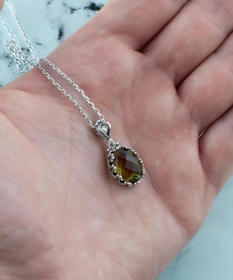 May include: A silver chain necklace with a green gemstone pendant. The pendant is oval shaped and has a detailed silver frame.