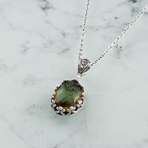 May include: A silver chain necklace with a green and brown oval gemstone pendant set in a silver filigree frame.