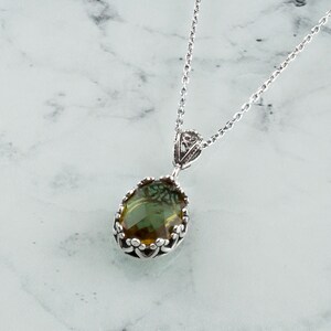 May include: A silver chain necklace with a green and brown oval gemstone pendant set in a silver filigree frame.