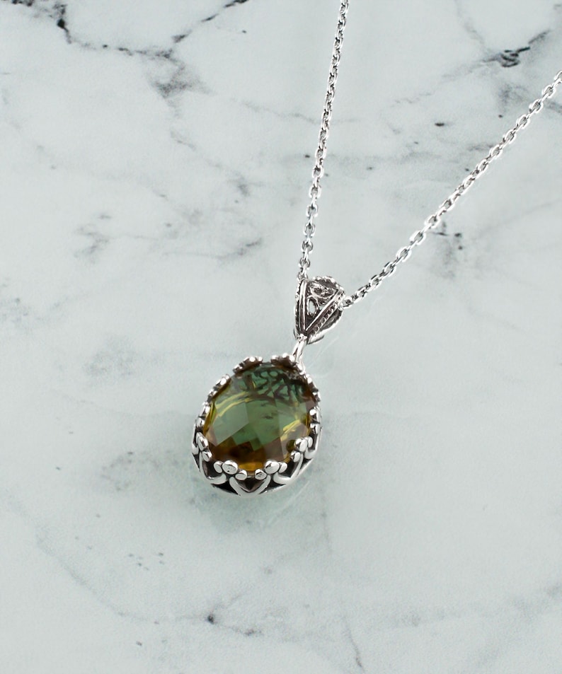 May include: A silver chain necklace with a green and brown oval gemstone pendant set in a silver filigree frame.
