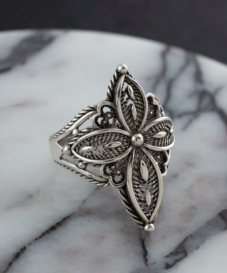 May include: A silver ring with a delicate, intricate floral design. The ring is made of sterling silver and features a filigree pattern.