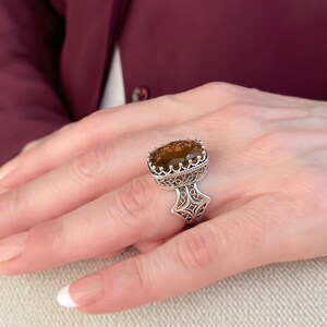 May include: A silver ring with a large, oval-shaped, brown gemstone set in a filigree design.