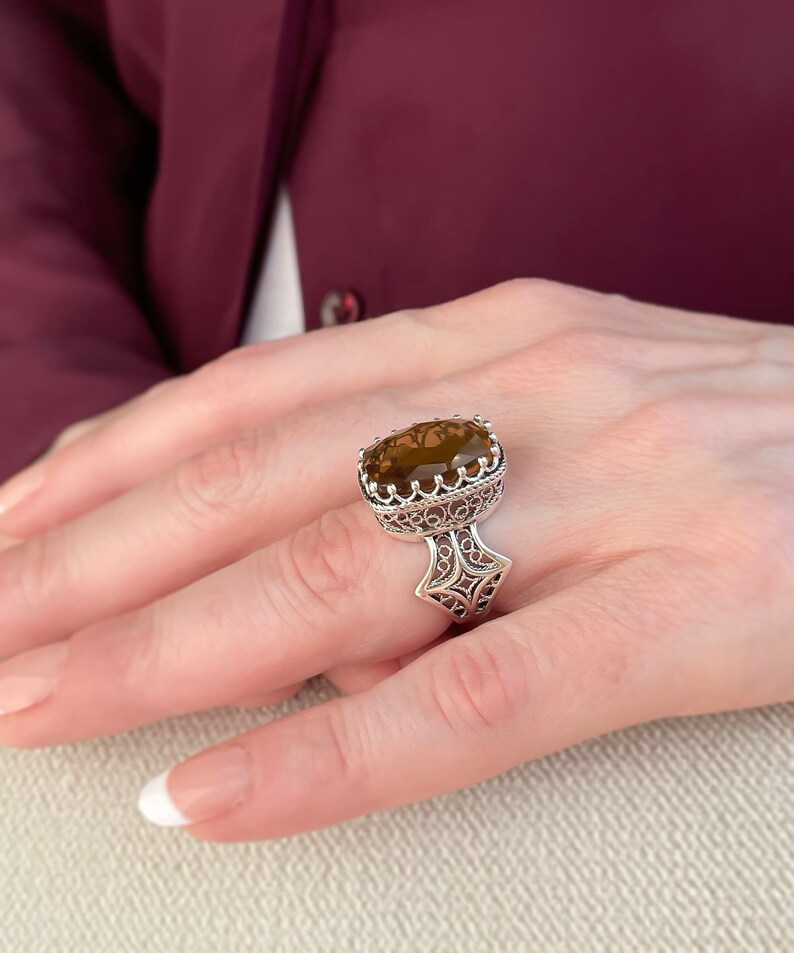 May include: A silver ring with a large, oval-shaped, brown gemstone set in a filigree design.