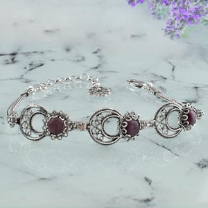 May include: A silver bracelet with three purple gemstone accents. The bracelet features a delicate filigree design.