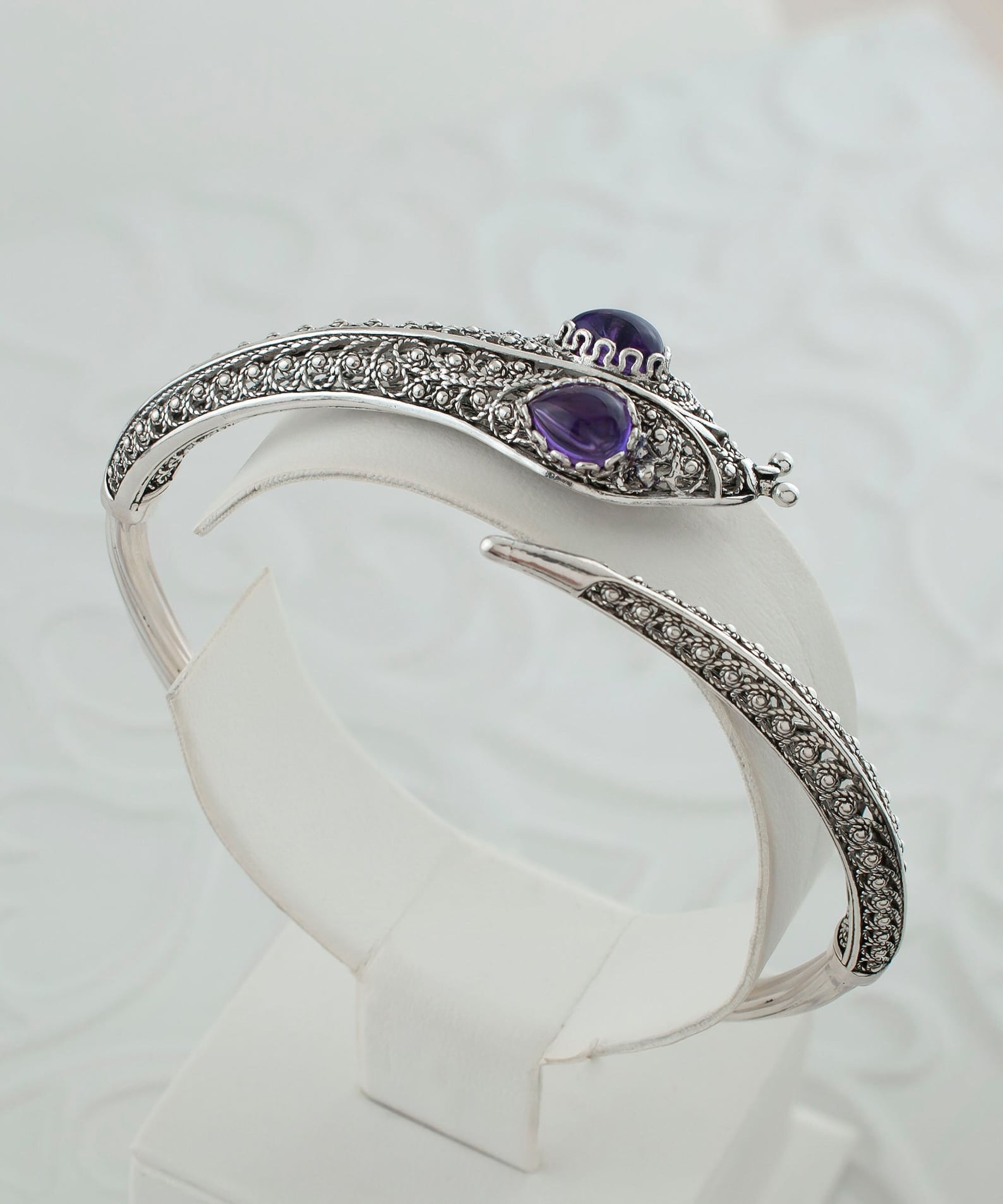 Silver gothic snake cuff bracelet with amethyst eyes and ornate filigree design on display stand