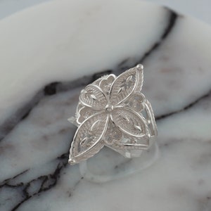 May include: A silver filigree ring with a flower design. The ring is delicate and intricate, with a floral pattern that is both elegant and whimsical.