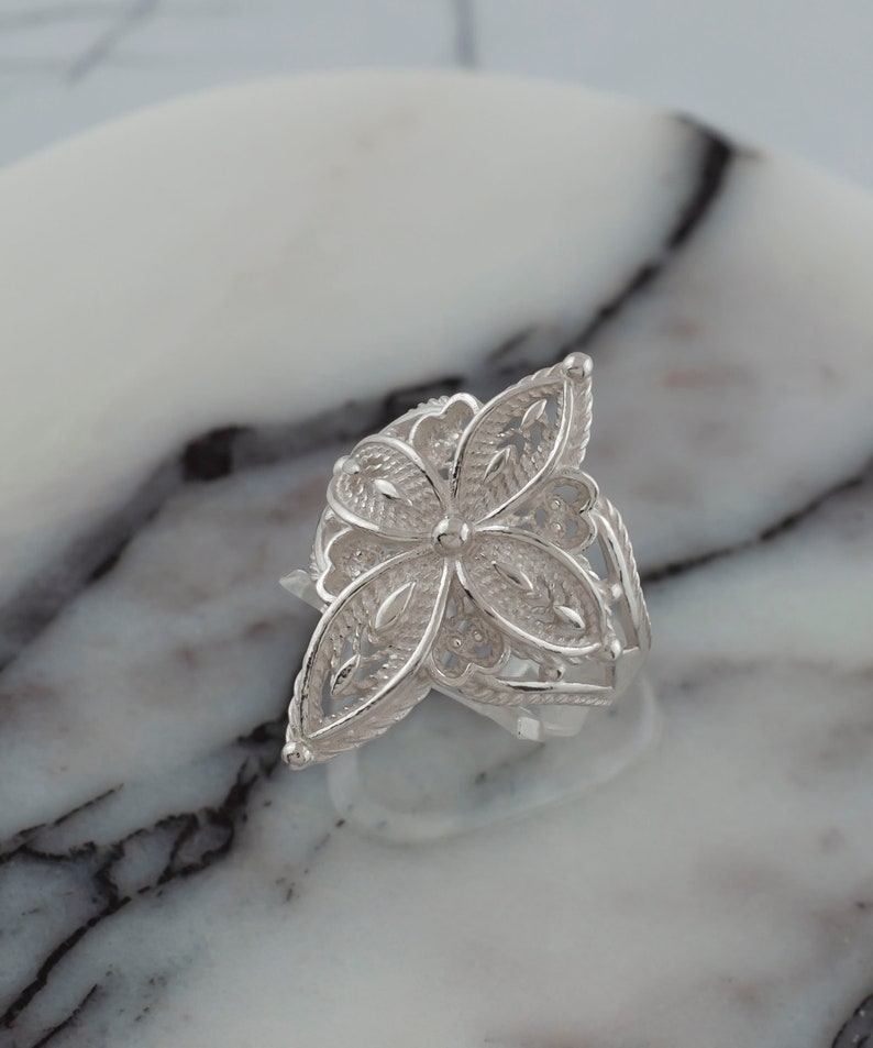 May include: A silver filigree ring with a flower design. The ring is delicate and intricate, with a floral pattern that is both elegant and whimsical.