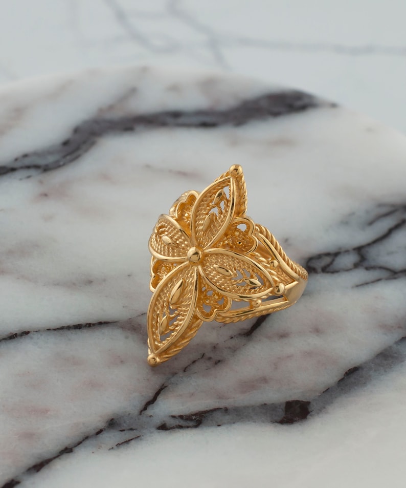 May include: A gold filigree ring with a floral design. The ring is made of intricate, delicate metalwork and has a triangular shape.